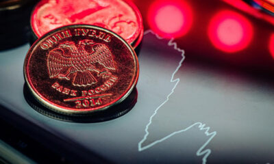 Close-up of a 2014 Russian ruble coin with an eagle, resting on a glossy surface beside a white outline map of Russia and red neon lights.