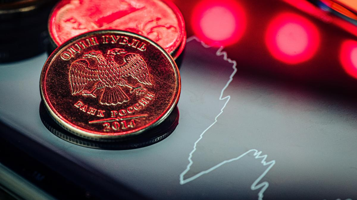 Close-up of a 2014 Russian ruble coin with an eagle, resting on a glossy surface beside a white outline map of Russia and red neon lights.