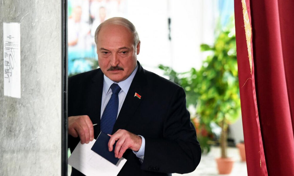Older man in a dark suit and blue tie places a ballot into a voting box at a polling station.