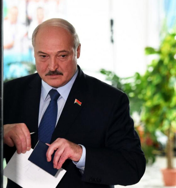 Older man in a dark suit and blue tie places a ballot into a voting box at a polling station.