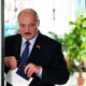 Older man in a dark suit and blue tie places a ballot into a voting box at a polling station.