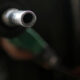 Metal fuel nozzle pointed toward the camera at a gas station, with a blurred background of a person holding the hose