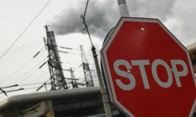 Red stop sign in the foreground with power lines and a smokestack emitting smoke in an industrial area.