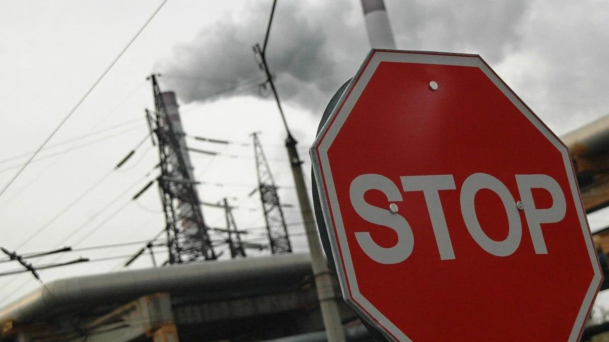 Red stop sign in the foreground with power lines and a smokestack emitting smoke in an industrial area.