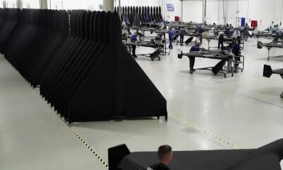 Spacious factory floor with long rows of black fabric panels and workers at workbenches assembling components.