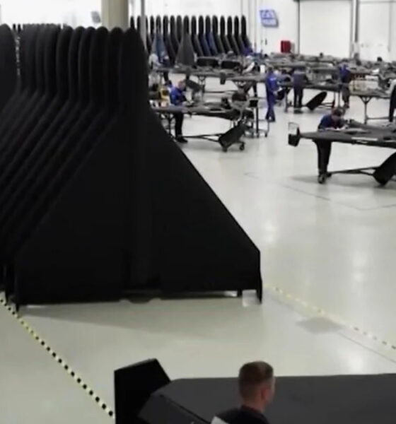 Spacious factory floor with long rows of black fabric panels and workers at workbenches assembling components.