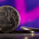 Close-up of a 1 ruble coin standing on edge with a purple blurred background on the shiny surface.