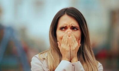 Woman with hands over her mouth, appearing shocked or anxious outdoors.
