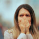 Woman with hands over her mouth, appearing shocked or anxious outdoors.