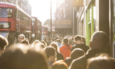 Crowded city street with red double-decker buses and pedestrians in sunlight near a shopfront (Primark).