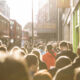 Crowded city street with red double-decker buses and pedestrians in sunlight near a shopfront (Primark).