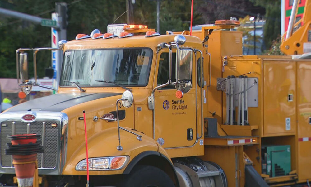 Yellow Seattle City Light utility truck with equipment and crane on a road.