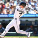 Baseball batter in a white uniform swinging a bat during a game with a blurred crowd in the background.