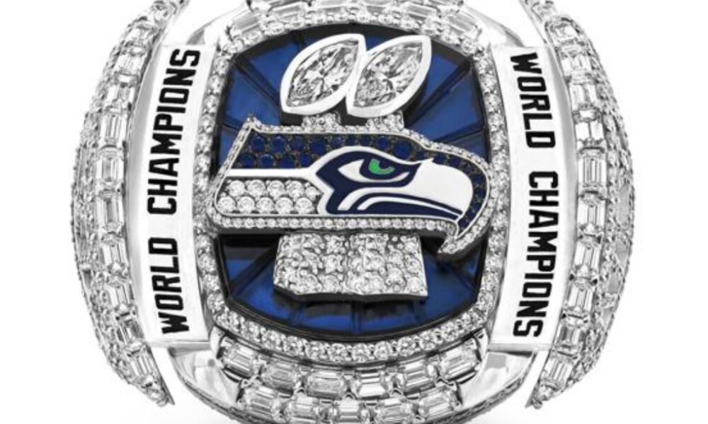 Diamond-encrusted Seattle Seahawks World Champions ring with blue background and surrounding “World Champions” inscriptions.