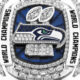 Diamond-encrusted Seattle Seahawks World Champions ring with blue background and surrounding “World Champions” inscriptions.