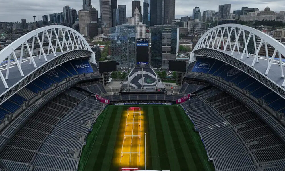 Aerial view of a large stadium with a green field and a yellow central court, city skyline in the background.” but we must remove smart quotes.