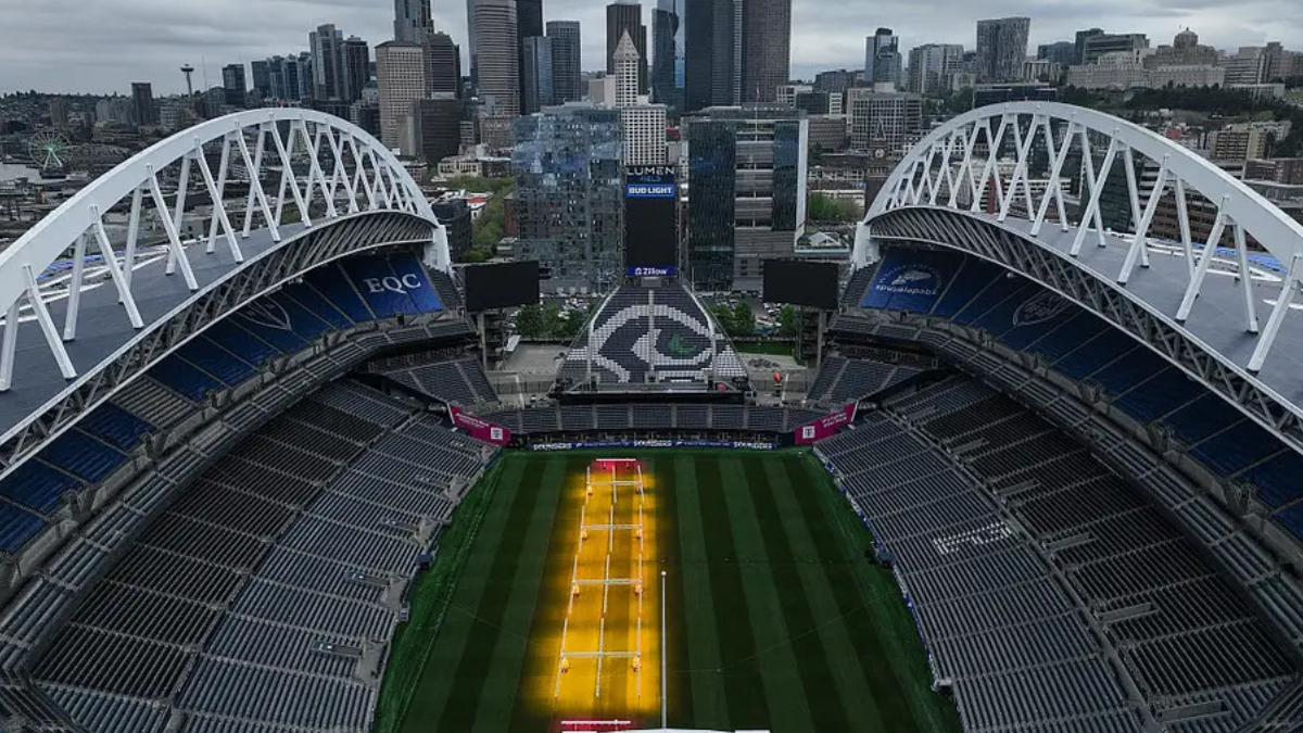Aerial view of a large stadium with a green field and a yellow central court, city skyline in the background.” but we must remove smart quotes.