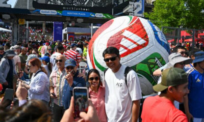 Crowd at an outdoor festival with a giant inflatable soccer ball centerpiece in the background.