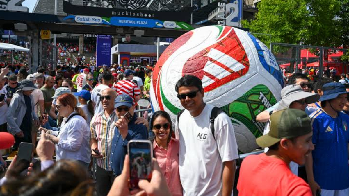 Crowd at an outdoor festival with a giant inflatable soccer ball centerpiece in the background.