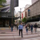 Pedestrians cross a city street at a wide crosswalk in front of Barnes & Noble; a white bus is on the right side.