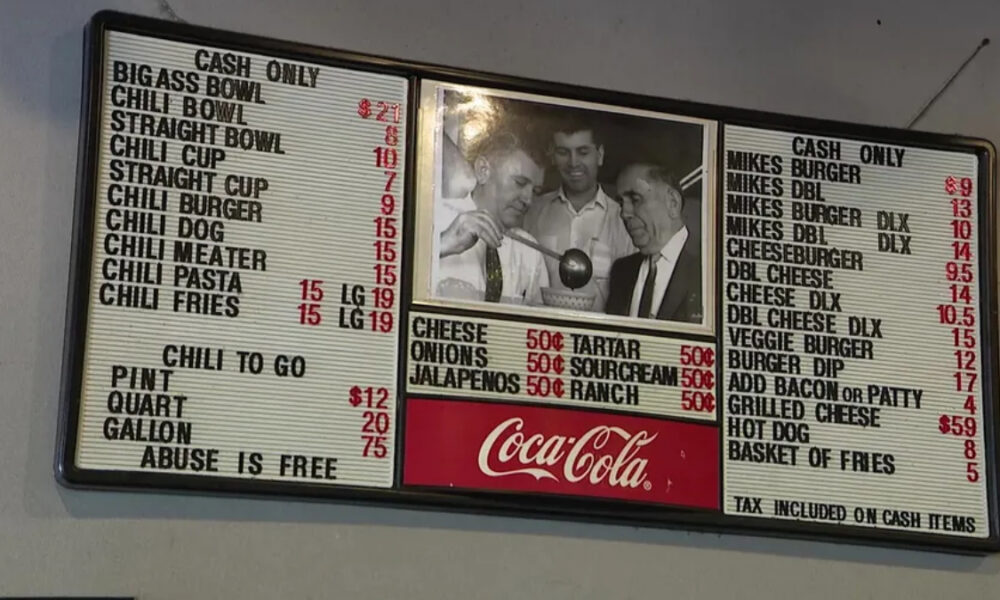 Old-fashioned diner menu board with prices for chili, burgers and sides, black-and-white photo in the center, Coca-Cola sign at bottom right/centermost area.