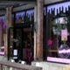 Exterior of a donut shop with pink Donuts & Coffee sign, wooden posts, and white outdoor chairs outside.