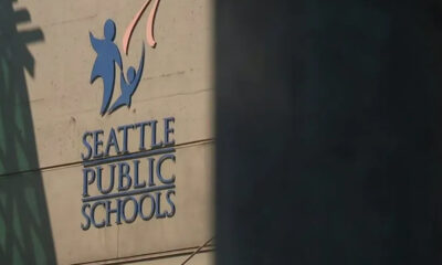 Seattle Public Schools sign on a concrete wall with a blue abstract logo of two figures raised in the air.