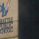 Seattle Public Schools sign on a concrete wall with a blue abstract logo of two figures raised in the air.