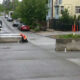Two workers in orange safety vests repair a curb on a residential street, with barriers and equipment nearby.