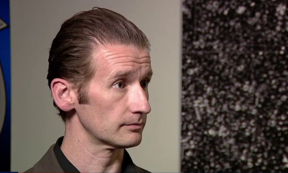 Man with slicked-back hair in a close-up profile during an interview setting