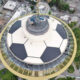 Aerial view of a circular observation tower with a ring walkway atop a city blocked by trees and buildings nearby.