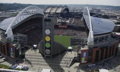 Aerial view of a packed outdoor stadium during a game, with a tall tower displaying colored circular panels in the foreground.