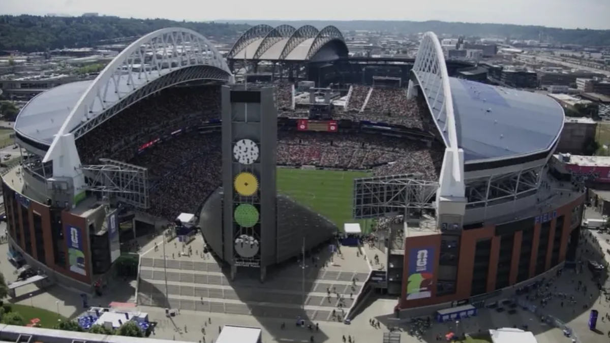 Aerial view of a packed outdoor stadium during a game, with a tall tower displaying colored circular panels in the foreground.