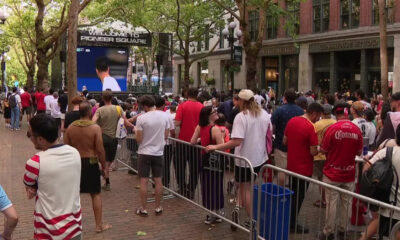 Crowd gathered behind metal barricades watching a large outdoor screen at a street event in Pioneer Square.