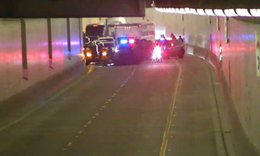 Emergency vehicles with flashing red and blue lights in a dim tunnel, blocking the road at the far end.