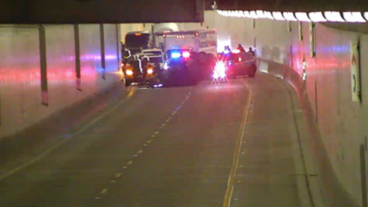 Emergency vehicles with flashing red and blue lights in a dim tunnel, blocking the road at the far end.