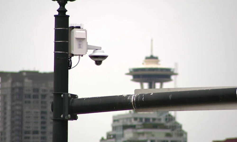 Outdoor security camera mounted on a metal street pole with a city skyline and a distinctive tower in the background