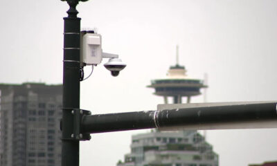 Outdoor security camera mounted on a metal street pole with a city skyline and a distinctive tower in the background