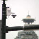 Outdoor security camera mounted on a metal street pole with a city skyline and a distinctive tower in the background