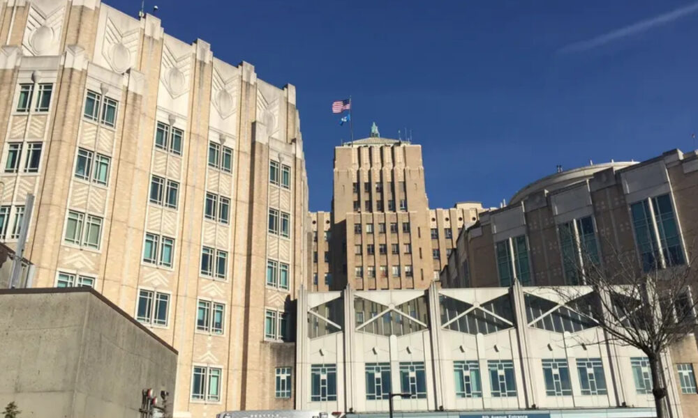 A large beige brick government-style building with an American flag atop a central tower under a clear blue sky.