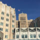 A large beige brick government-style building with an American flag atop a central tower under a clear blue sky.