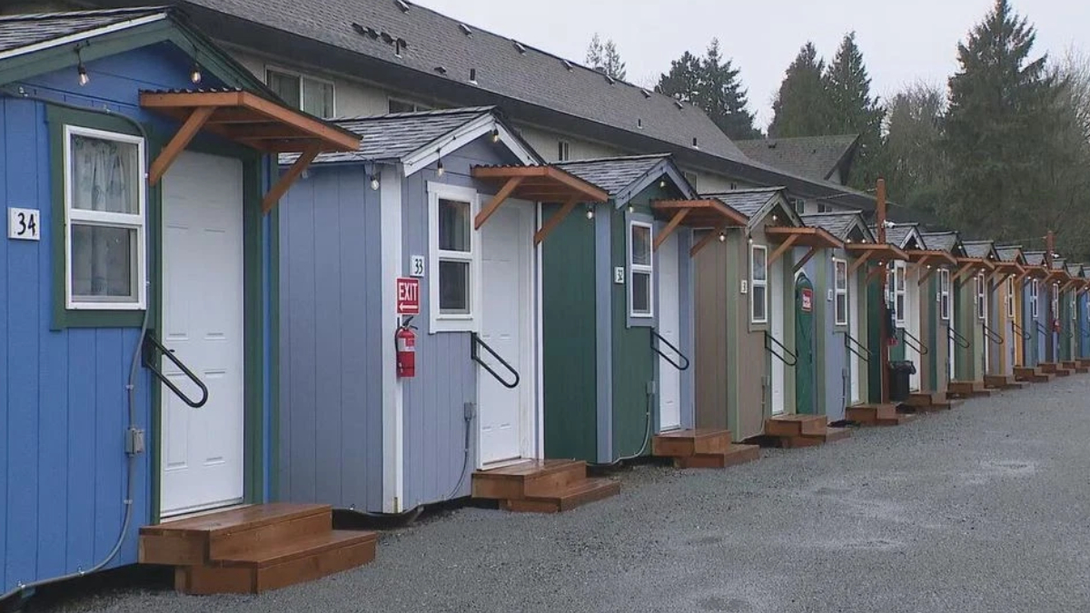 Row of colorful small cabins with white doors, wooden steps, string lights, and a gravel path