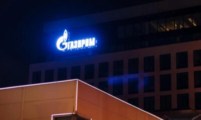 Blue Gazprom sign glowing on a dark building at night, with neon-lit foreground edge.