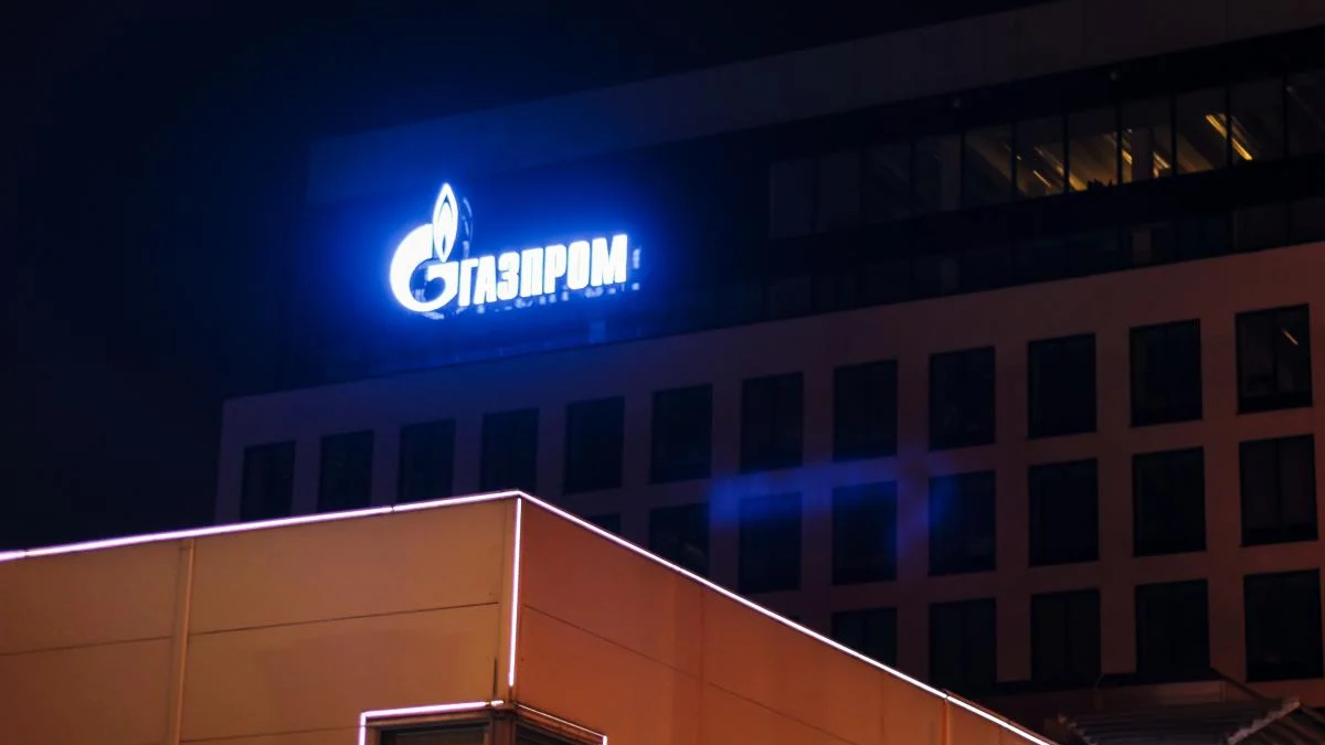 Blue Gazprom sign glowing on a dark building at night, with neon-lit foreground edge.
