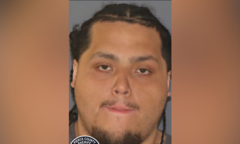 Mugshot of a man with braided hair and goatee against a gray background; a sheriff badge is partially visible in the corner.