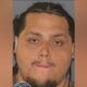 Mugshot of a man with braided hair and goatee against a gray background; a sheriff badge is partially visible in the corner.