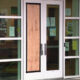 Glass double doors with a plywood panel taped over the center; entry blocked, with notices on the glass and a brick exterior wall nearby, plus a bright green scooter to the right.