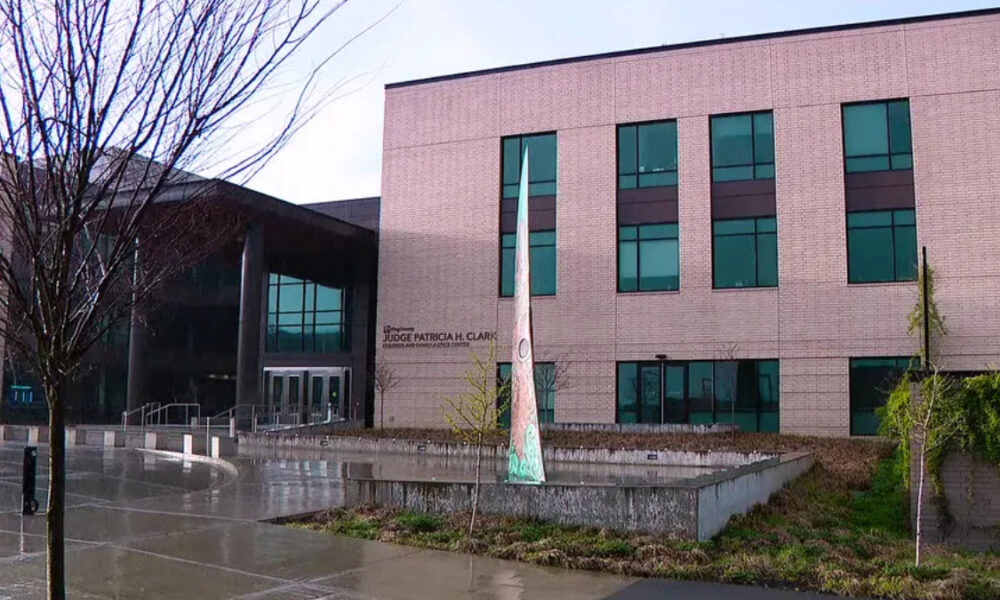 Modern brick building with glass entrance and a tall white banner sculpture in a shallow reflecting pool in front, after rain.