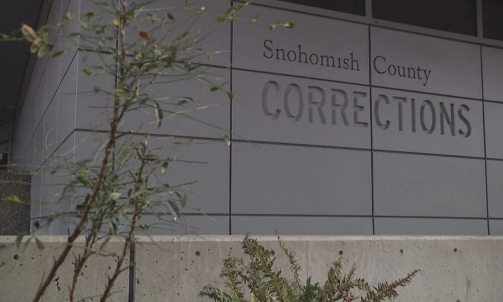 Exterior view of Snohomish County Corrections building with large raised lettering on gray panels and some plants in the foreground.