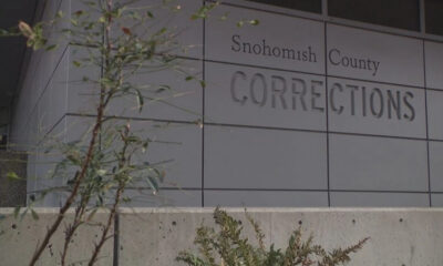 Exterior view of Snohomish County Corrections building with large raised lettering on gray panels and some plants in the foreground.